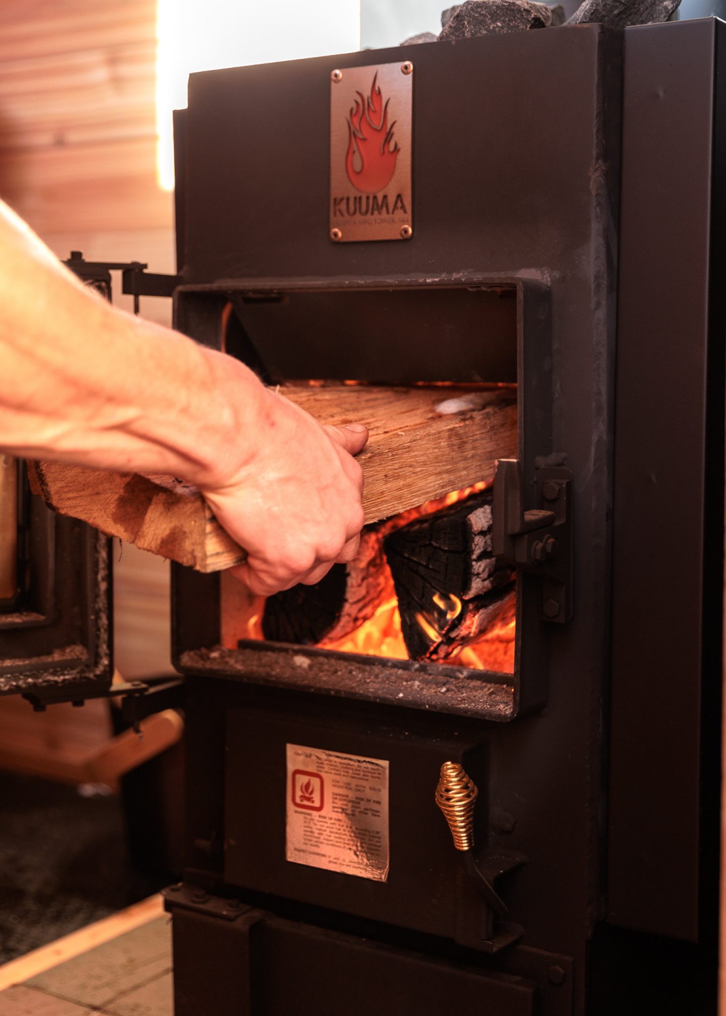 Putting wood into the Kuuma Stove inside a mobile rental sauna in Minnesota
